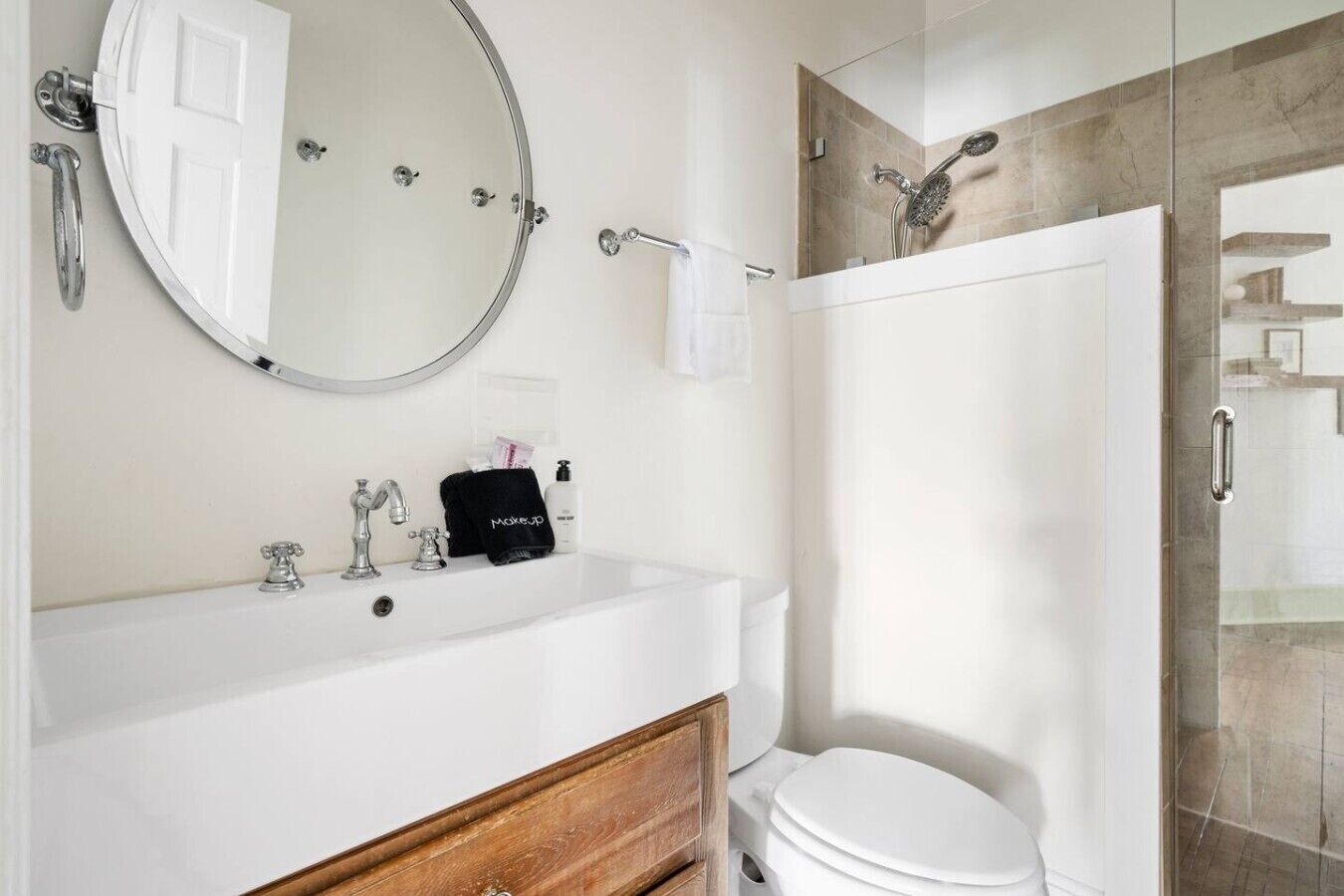 A modern bathroom with a white sink, a round mirror, a handheld showerhead, and a toilet.