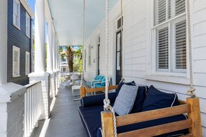 A porch with a swing, a table with chairs, and a view of a building. - 2BR Spring Street Retreat - B (Charleston)