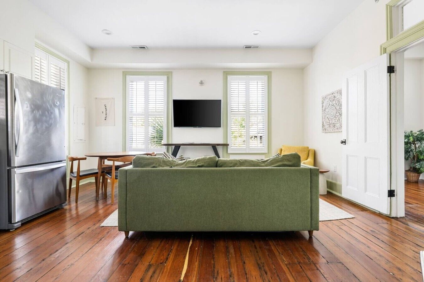 Uma sala de estar com sofá, televisão de tela plana, mesa de jantar de madeira e geladeira.