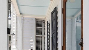 Un pasillo estrecho con una puerta de madera, una silla blanca y un taburete estampado.