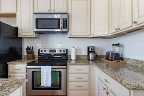 A kitchen with a stainless steel microwave, a stove, a coffee maker, and a blender on the countertop. - 1 BR Cottage with Parking - Charleston Charm (Charleston)