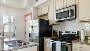 Una cocina con un refrigerador de acero inoxidable, un microondas, un horno y una encimera de granito.