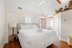 A bedroom with a large bed, two bedside lamps, a wooden floor, and a ceiling fan. - 1 BR Cottage with Parking - Charleston Charm (Charleston)