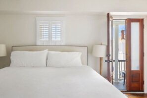 A bed with white linens, a window with shutters, and a door leading to an outdoor area. - 1 BR Cottage with Parking - Charleston Charm (Charleston)