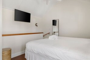 A hotel room with a bed, a TV mounted on the wall, a wooden headboard, a bedside table, and a mirror. - 1 BR Cottage with Parking - Charleston Charm (Charleston)
