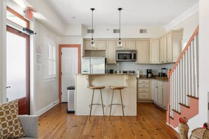 Une cuisine moderne dotée d'un îlot central, de tabourets de bar, d'un four à micro-ondes et d'un escalier avec une rampe rose.