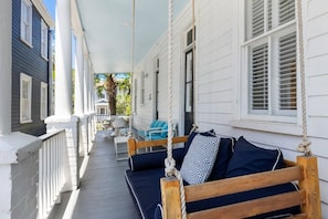 Eine Veranda mit einer Schaukel, einem Tisch mit Stühlen und Blick auf ein Gebäude.