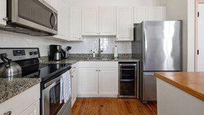 A kitchen with white cabinets, a stainless steel refrigerator, a microwave, a stove, and a wooden countertop. - 2BR Spring Street Escape - D (Charleston)