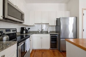 Eine Küche mit weißen Schränken, einem Edelstahl-Kühlschrank, einer Mikrowelle, einem Herd und einer Holz Arbeitsplatte.