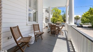 En veranda med et bord og stole, et hvidt gelænder og udsigt til gaden.