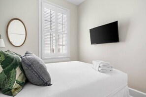 Une chambre d’hôtel avec un lit, une télévision, une fenêtre avec des stores et un miroir.