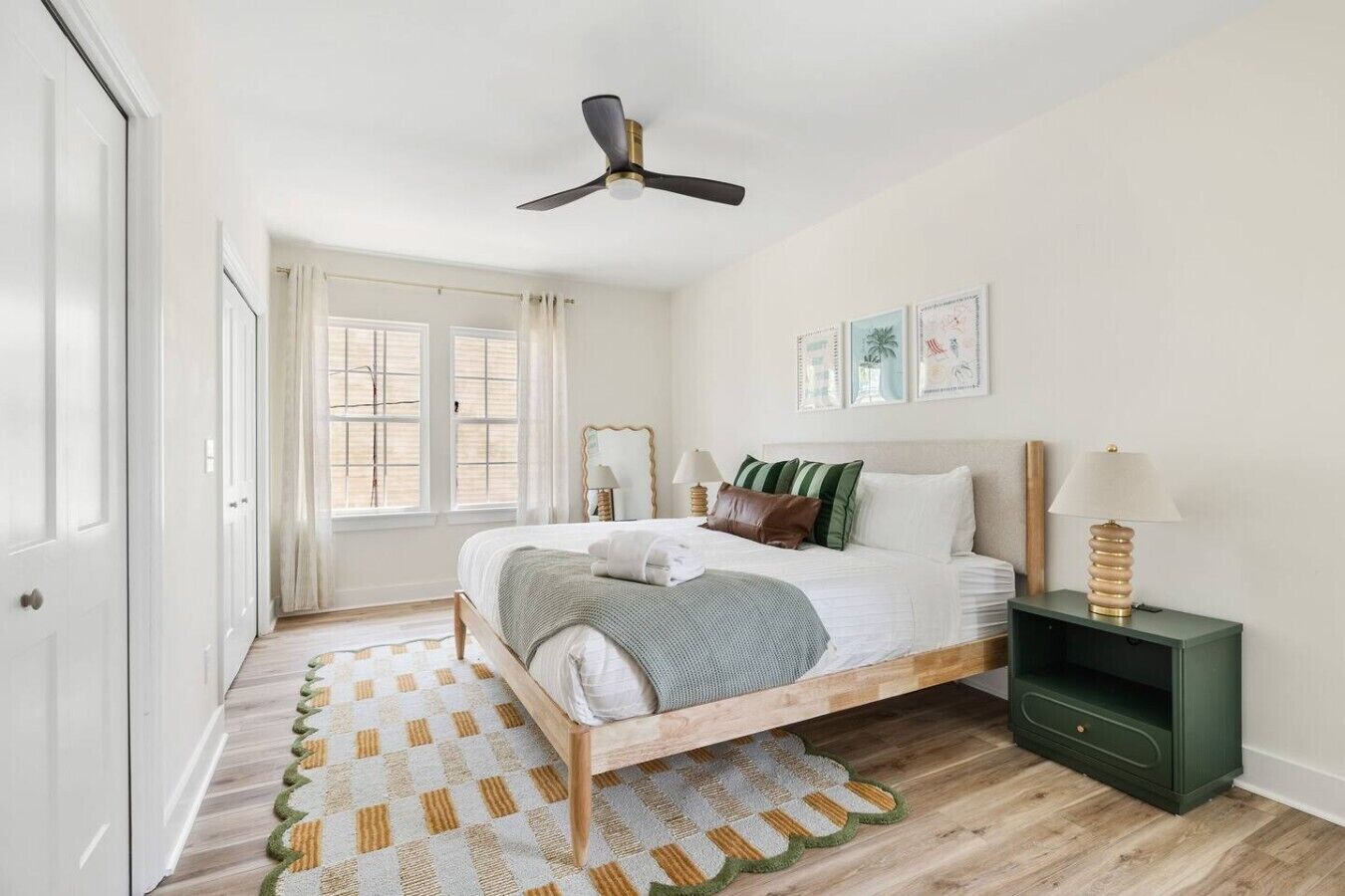 Un dormitorio con cama, mesitas de noche, ventilador de techo y ventana con cortinas.