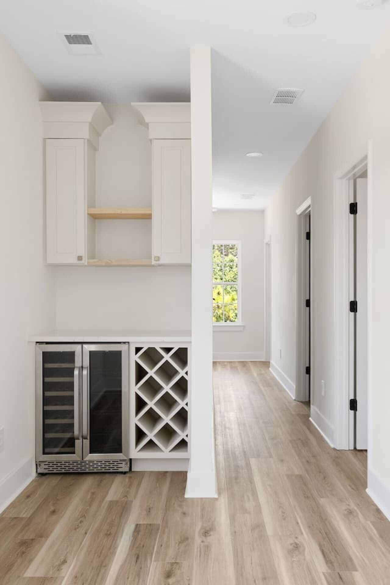 A hallway with wooden flooring, white walls, and a built-in wine rack.