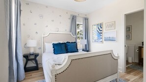 Ein Schlafzimmer mit Bett, Vorhängen, Nachttisch, Lampe und Wandbildern.