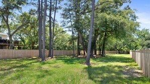 Ein umzäunter Garten mit hohen Bäumen und einer Holzterrasse.