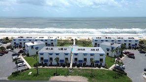 Un hotel frente a la playa con varias edificaciones, un estacionamiento y vistas al océano.
