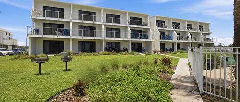 A multi-story hotel with a central courtyard, outdoor seating, and a pathway leading to the entrance.