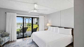 Une chambre d’hôtel avec un grand lit, un ventilateur de plafond, une vue sur l’extérieur, une chaise et une lampe.