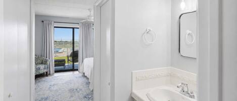 A hotel room with a balcony, a bathroom with a sink and mirror, and a view of the outside.