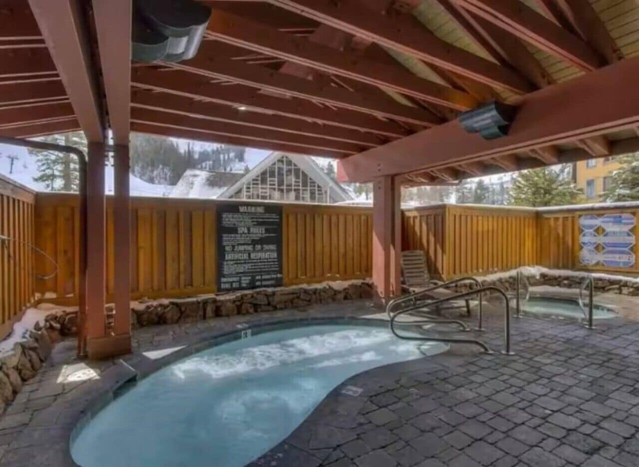 An outdoor hot tub area with a wooden deck, stone walls, and a signboard.