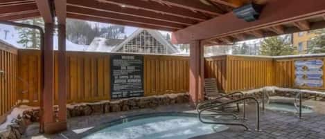 An outdoor hot tub area with a wooden deck, stone walls, and a signboard.