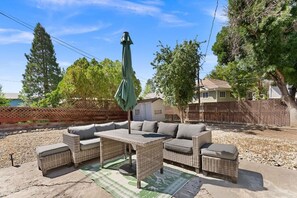 Eine Terrasse im Freien mit Korbmöbeln, einem Tisch und einem Sonnenschirm.