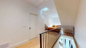 A modern interior with a staircase, a bed with orange bedding, and a skylight.