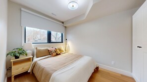 Een slaapkamer met een bed, nachtkastje, lamp en een raam.