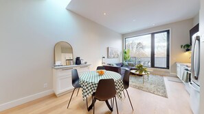 A modern kitchen with white cabinets, a large window, and a dining area with a checkered tablecloth and chairs.