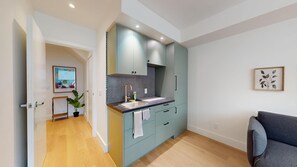 A modern kitchen with a central island, a dining area with a grey sofa, and a hallway leading to another room.