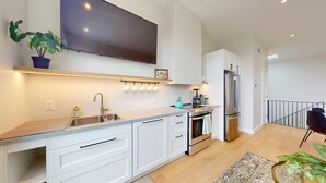 A modern kitchen with a flat-screen TV, stainless steel appliances, and white cabinetry.