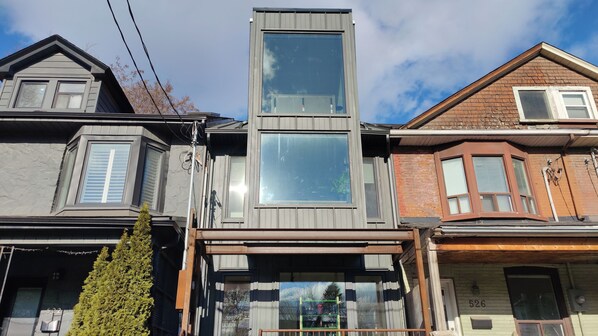 A row of three-story houses with distinct architectural styles, including a central house with a large glass window and a smaller house with a bay window.