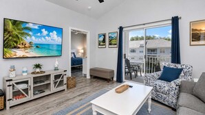 A modern living room with a flat-screen TV, a sofa, a coffee table, and a balcony with a view of a house. - Golf, Pool & Coastal Comfort Willow Bend 234 (North Myrtle Beach)