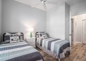 Ein Schlafzimmer mit zwei Betten, jeweils mit gestreifter Bettdecke und passenden Kissen, einem Nachttisch mit Lampe und einem Deckenventilator.