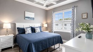 A bedroom with a bed, nightstands, a ceiling fan, a window with curtains, and a wall-mounted artwork. - Golf, Pool & Coastal Comfort Willow Bend 234 (North Myrtle Beach)