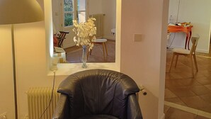 A living room with a black leather chair, a floor lamp, a vase with white flowers, and a large mirror reflecting the room. - Stunning villa with a pool and ocean view, Mediterranean garden, sleeps 8 (Grasse)