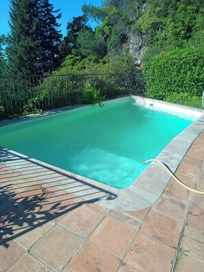 Ein rechteckiger Swimmingpool mit klarem, blauem Wasser, umgeben von einem Metallzaun und Steinfliesen.