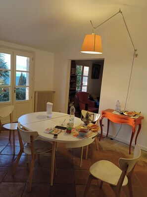 A dining area with a round table, chairs, a lamp, and a view through a window. - Stunning villa with a pool and ocean view, Mediterranean garden, sleeps 8 (Grasse)