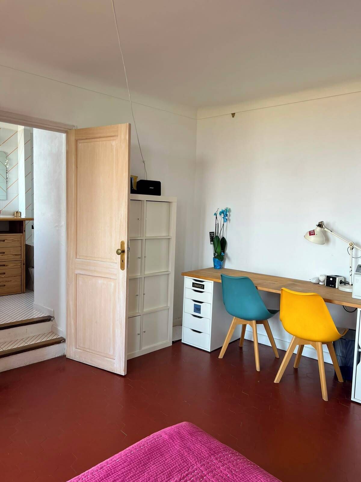 A room with a wooden desk, two chairs, a white wardrobe, and a pink rug.