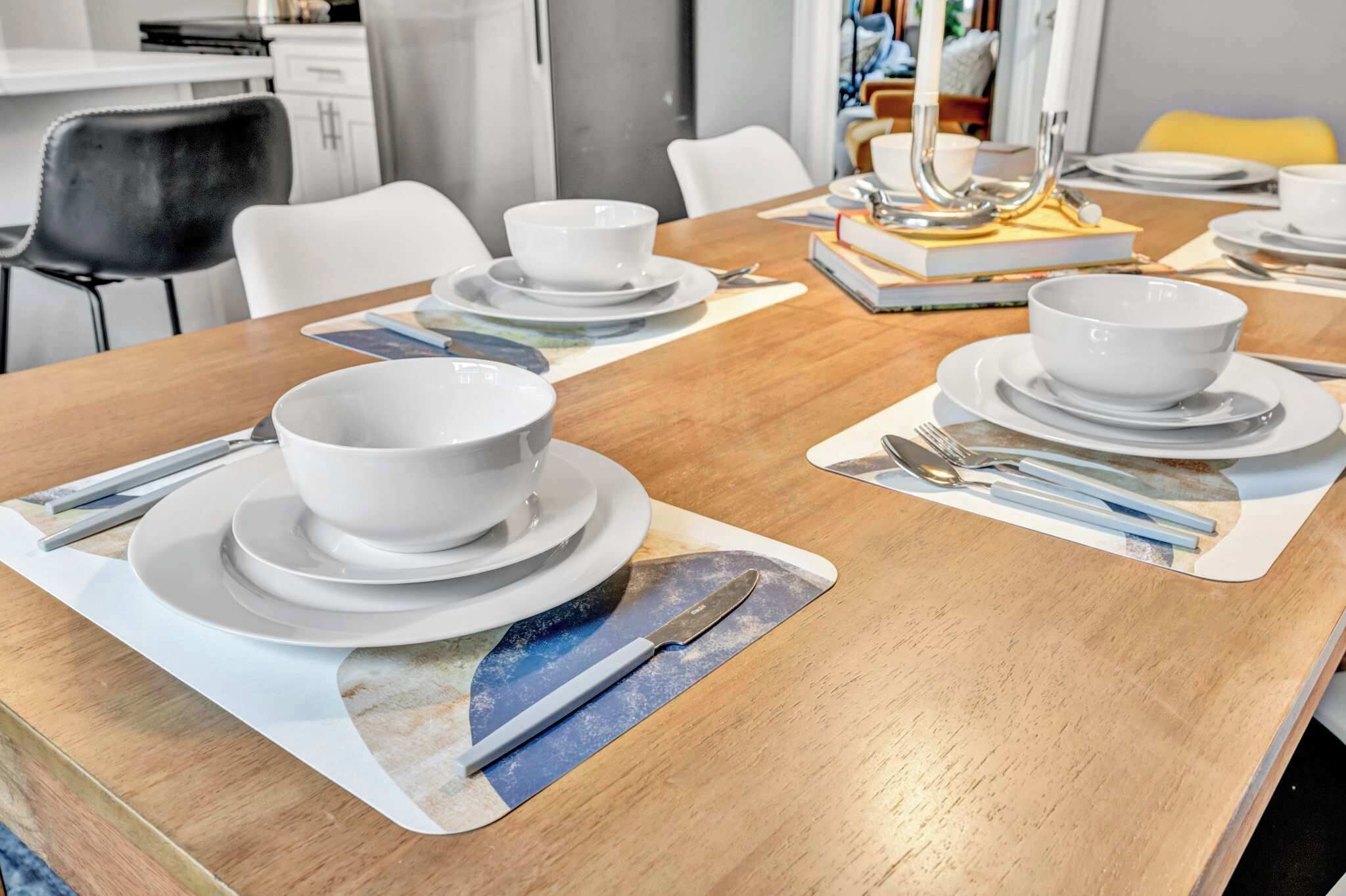 A dining table set with white plates, bowls, and cutlery, with a candle holder and books on the table.