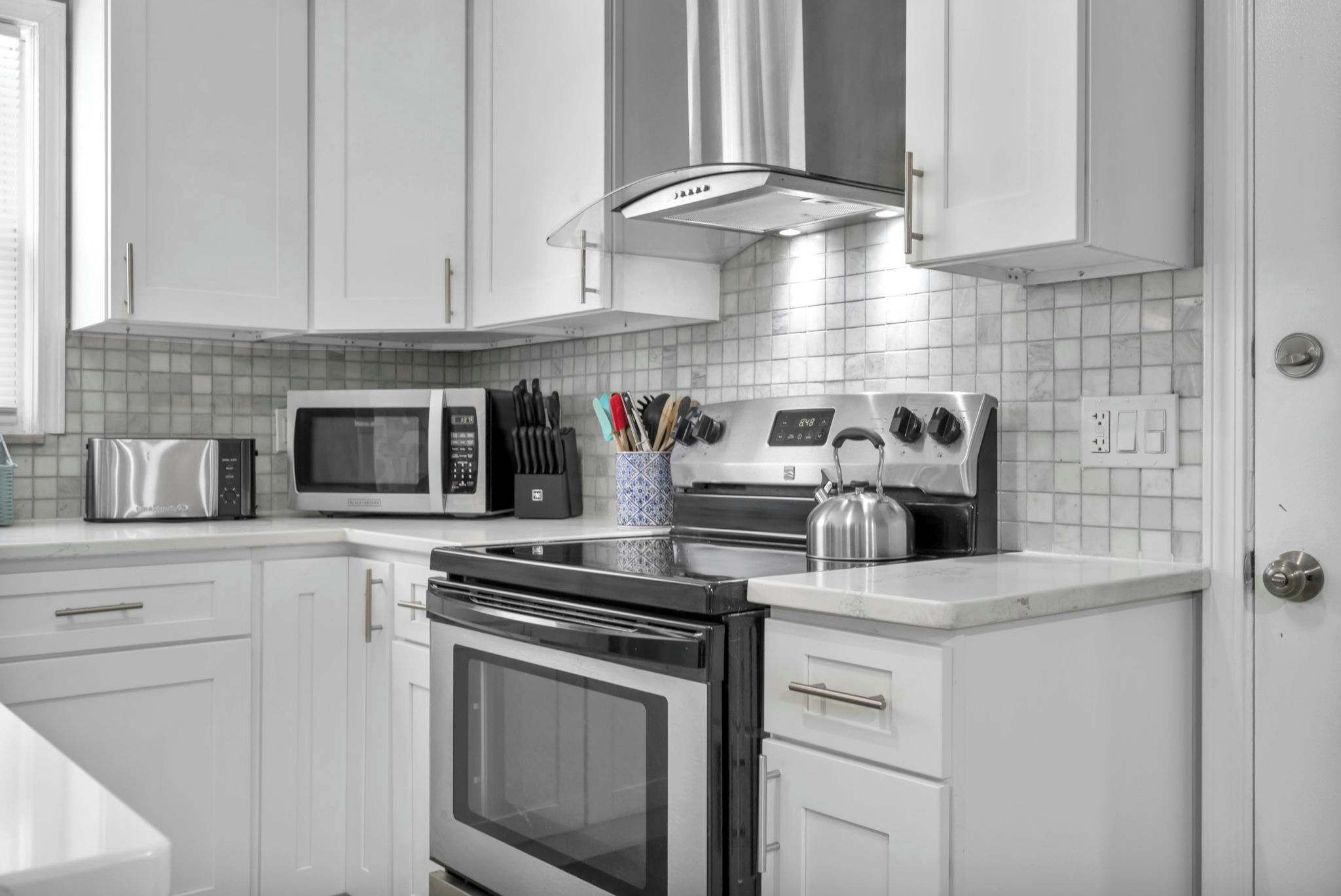 Cozinha moderna com armários brancos, eletrodomésticos de aço inoxidável e painel de azulejos.