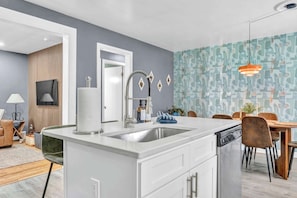 Una cocina moderna con una isla central, un comedor con mesa y sillas de madera, y una pared con diseño.