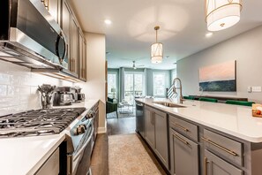 A modern kitchen with stainless steel appliances, a large island with a sink, and a view to a balcony. - East Nashville Social House | Sleeps 10 + Deck (Nashville)