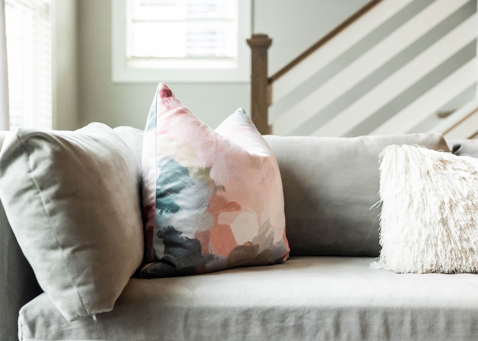 A sofa with two pillows, one with a floral pattern and another fluffy white one.