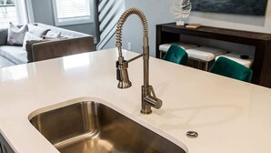 Eine Küche mit Spüle aus Edelstahl, einem gebogenen Wasserhahn und einer weißen Arbeitsplatte.