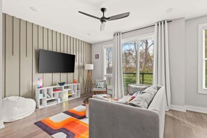 A modern living room with a flat-screen TV, a ceiling fan, a white bean bag, a grey sofa, and a colorful rug. - Nashville Pop Art 4BR, Near Downtown and Sleeps 10 (Nashville)