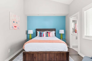 A bedroom with a bed, bedside lamps, a blue accent wall, and a door leading to another room. - Nashville Pop Art 4BR, Near Downtown and Sleeps 10 (Nashville)