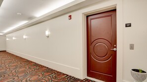 A hallway with a patterned carpet, a wooden door with a circular design, and a potted plant on the right. - Beachfront 1BR Apartment on Ocean Drive (Miami Beach)