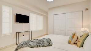 A bedroom with a bed, a TV mounted on the wall, a bedside table, and a window. - Beachfront 1BR Apartment on Ocean Drive (Miami Beach)