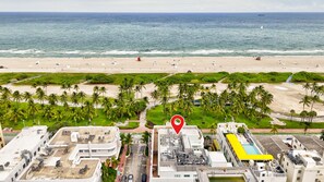 An aerial view of a coastal area with a beach, palm trees, and buildings. - Beachfront 1BR Apartment on Ocean Drive (Miami Beach)
